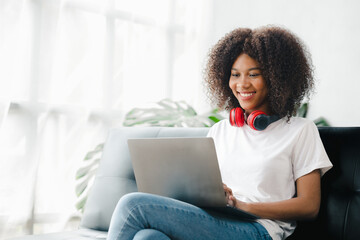 An American woman sits on the sofa on her laptop, spends her weekends on social media, watching movies and listening to music at home. Holiday concept.