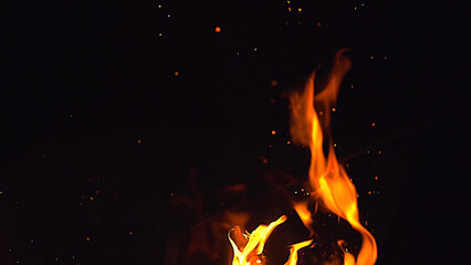 Fire flames and a lot of bright sparks are flying from the fire at night - obrazy, fototapety, plakaty