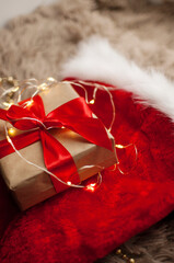 a gift in kraft paper and with a red ribbon of blue color on a Christmas red hat on a background of a golden garland in a vertical format