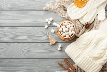 Winter holidays concept. Top view photo of headwear mittens plaid cup of cocoa with marshmallow serving mat decorative clip anise cinnamon sticks and dried orange slices on grey wooden desk background