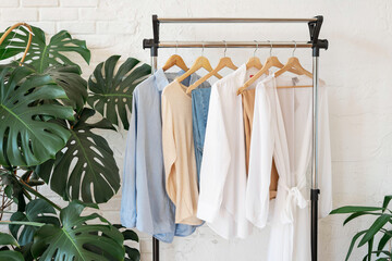 Trendy capsule wardrobe in beige and light blue on a rail rack against the background of a white...
