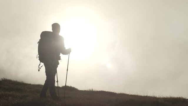 A hiker with a backpack climbs a mountain at sunset. Slow motion video of a tortured man climbing to the top of a mountain. The concept of freedom and happiness alone. High quality 4k footage