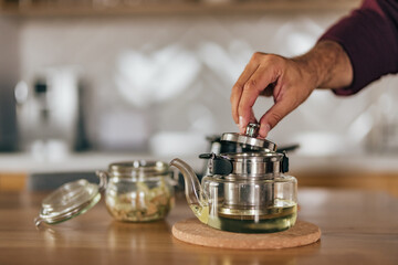 Focus on the teapot, man drinking tea at home, enjoying.