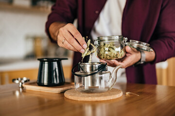 A man putting a dried herb tea into the teapot, with boiled water.