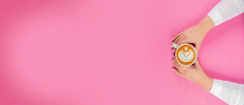 Woman's hands holding cup of coffee, top view of woman's hands holding cup of coffee. Isolated pink background with copy space. Beautiful latte art design element coffee shop menu concept idea.
