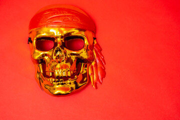 a golden skull with a red headband on a red background. Halloween, piracy. Jolly Roger. The sign of...