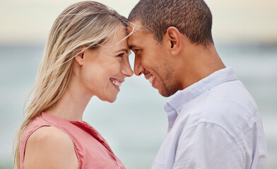 Fototapeta premium Portrait of couple at the beach with their forehead touching. Multiracial man and woman in relationship, happy, smiling and in love on vacation. Bonding, love and quality time together