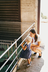 Mom and little daughter stand near paddock with goats in a farm. High quality photo