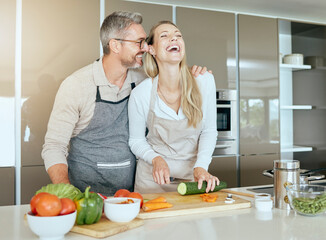 Couple in kitchen cooking together in their home, having fun and laughing. Middle aged man and woman cutting healthy vegetables and making food in their house. Smiling, happy and in love people