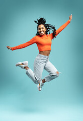 Excited happy pretty girl in casual jeans clothes high jump with raised hands and legs, on blue...