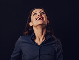 Beautiful funny toothy laughing business woman with wide open mouth looking up in blue shirt on black background with empty copy space for text. Closeup
