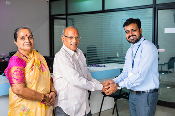 Fototapeta premium Happy smiling banker greeting by shaking hand to senior couple at bank - concept of financial support, banking adviser and consultation.
