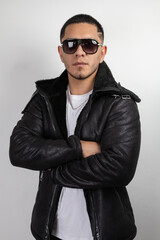 young model with short hair wearing sunglasses, leather sweater, jeans pants and white t-shirt with crossed arms, urban fashion and style, latin man