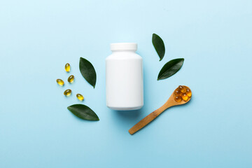 Omega-3 capsules lie in white bottle on a table with green leaves background. Fish oil tablets....