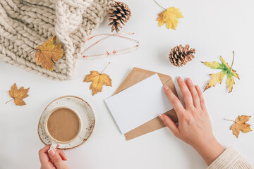 White and beige Autumn flat lay composition. Cup of coffee, scarf, glasses, cones, envelope and autumn leaves on white background.