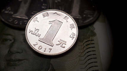 One Chinese Yuan close up. A 1 yuan coin lies on a 1 yuan bill. Several coins in the background