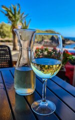 A glass and a carafe of white wine on a wooden table near beach Playa Charco del Conde without people in Valle Gran Rey, La Gomera, Canary Islands, Spain, Europe. Vacation vibes on tropical island