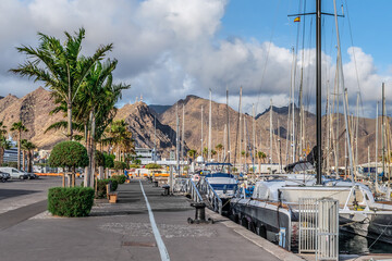 Santa Cruz de Tenerife, Spain - November 24, 2021: Promenade in the port of Santa Cruz de Tenerife. Many yachts are moored off the coast of the Atlantic Ocean against the backdrop of the mountains - Powered by Adobe