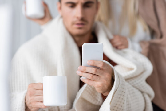 blurred man using smartphone and holding cup of tea near girlfriend.