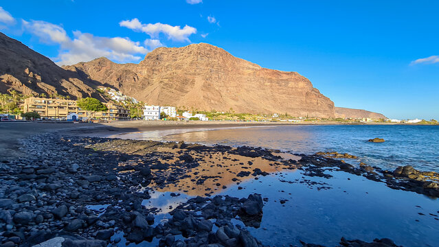 Scenic view on beach Playa Valle Gran Rey during sunset seen from Promenade de Playa de La Calera in Valle Gran Rey on La Gomera, Canary Islands, Spain, Europe. Reflections in dark volcanic sand beach