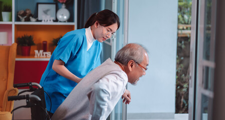 Asian senior elderly man patient doing physical therapy with caregiver. woman nurse helping get up from wheelchair for practice walking at home, practice walking slowly at nursing home care concept.