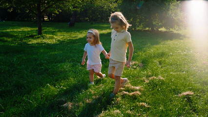 In a sunny day cute little kids brother and sister together walking together the grass in the park holding hands