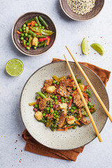 Wok with turkey meat, corn, green peas, green beans and carrots served on gray background with chopsticks. Asian food concept of street food