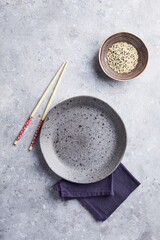 Empty grey round plate with chopsticks and linen napkin on gray background. Top view