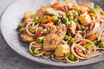 Wok with turkey meat, soba noodles, corn, green peas, green beans and carrots served on gray background . Asian food, concept of street food