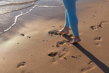 Close up woman legs walking on tropical sunset beach with smooth wave and bokeh sun light wave...