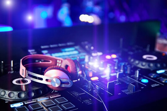 Pink DJ headphones on sound mixer and turntables in night club
