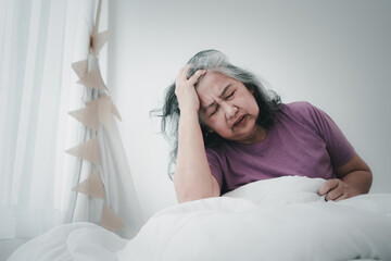 Unhealthy elderly senior Asian woman sitting on bed suffering from headache and migraine so pain...