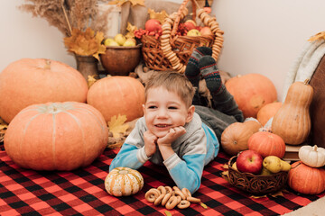 Fototapeta na wymiar A little boy lies on the floor near pumpkins and autumn fruits. Autumn Festival