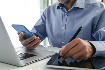 Closeup man hands using smartphone, laptop and tablet. Businessman works with computer, phone, pad