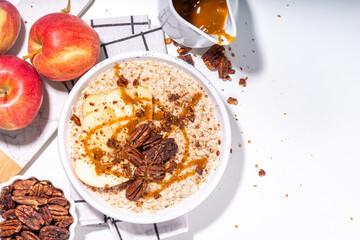 Simple autumn traditional American breakfast. Ready to eat apple pie oatmeal porridge with apples, pecans and caramel on white table background copy space