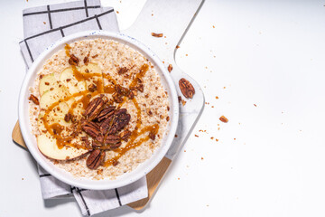 Simple autumn traditional American breakfast. Ready to eat apple pie oatmeal porridge with apples, pecans and caramel on white table background copy space