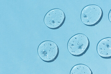 Drops of serum or hyaluronic acid gel on a blue background. Smears of cosmetic skin care products. Wellness and beauty concept.