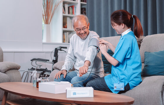 Asian Caregiver Doctor Examine Older Patient Use Blood Pressure Gauge. Nurse Visit And Taking Care Patient Senior Man Checkup Elderly Old Man In Living Room, Healthcare Insurance Concept.