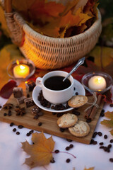 Autumn picnic with cup coffee with cookies and chocolate on background of burning candles in evening outdoors. Still life in garden with maple leaves on lawn