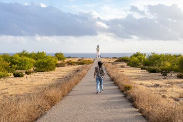 Obraz premium Young woman walks to a lighthouse in sunset