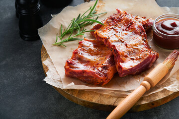 Pork ribs. Raw meat. Raw pork ribs in marinade with spices, rosemary, tomato sauce and garlic on old wooden stand on black stone table background. Barbecue concept. Selective focus. Mock up. - obrazy, fototapety, plakaty