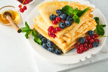 Pancakes. Stack of crepes or thin pancakes with berries, blueberries, red currants, raspberries and honey for breakfast. Homemade breakfast. Copy space. Selective focus.