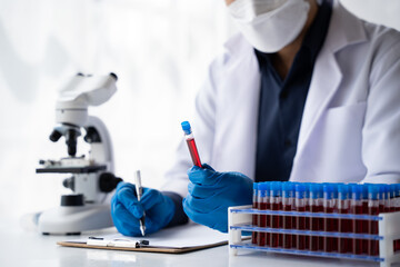 Doctor hand taking a blood sample tube from a rack with machines of analysis in the lab background,...