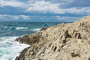 Fototapeta na wymiar rocky seashore formed by columnar basalt against the backdrop of a sea, coastal landscape of the Kuril Islands
