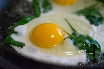 fried eggs in a frying pan with green spinach