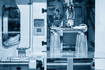 The robotic arm gripping the plastic cup from the injection machine.