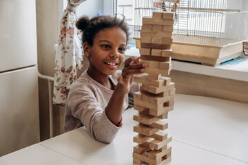Close-up of a happy African American girl playing jenga game on a table at home.Board games concept.Stay home concept.Selective focus.