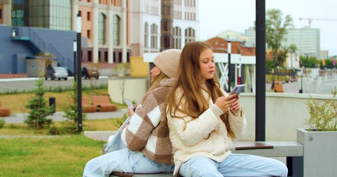 Modern addictions - two teenage girls are sitting buried in smartphones while walking outdoors in autumn time.