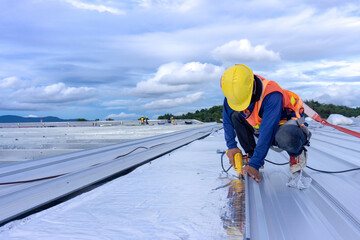 Worker wearing safety harness for installation metal roof sheet and Roof insulation at Warehouse roof © Kittisak