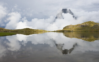 Sunset with the Midi dOssau mountain in the clouds reflected on the Ayous lakes, Pyrenees National Park, France.